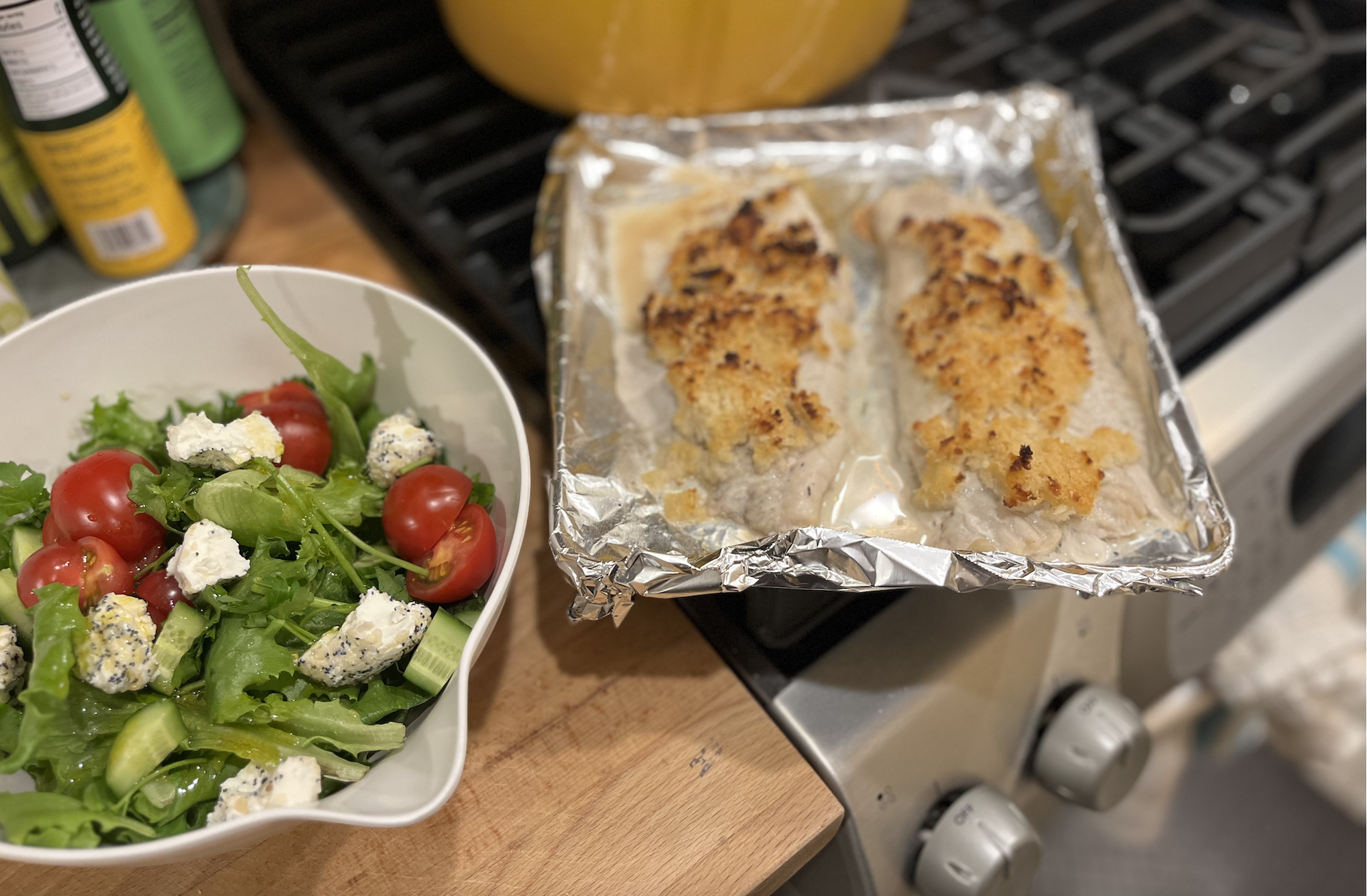 a bowl of salad with goat cheese and a baking tray with baked skate fish with some crunchy panko topping