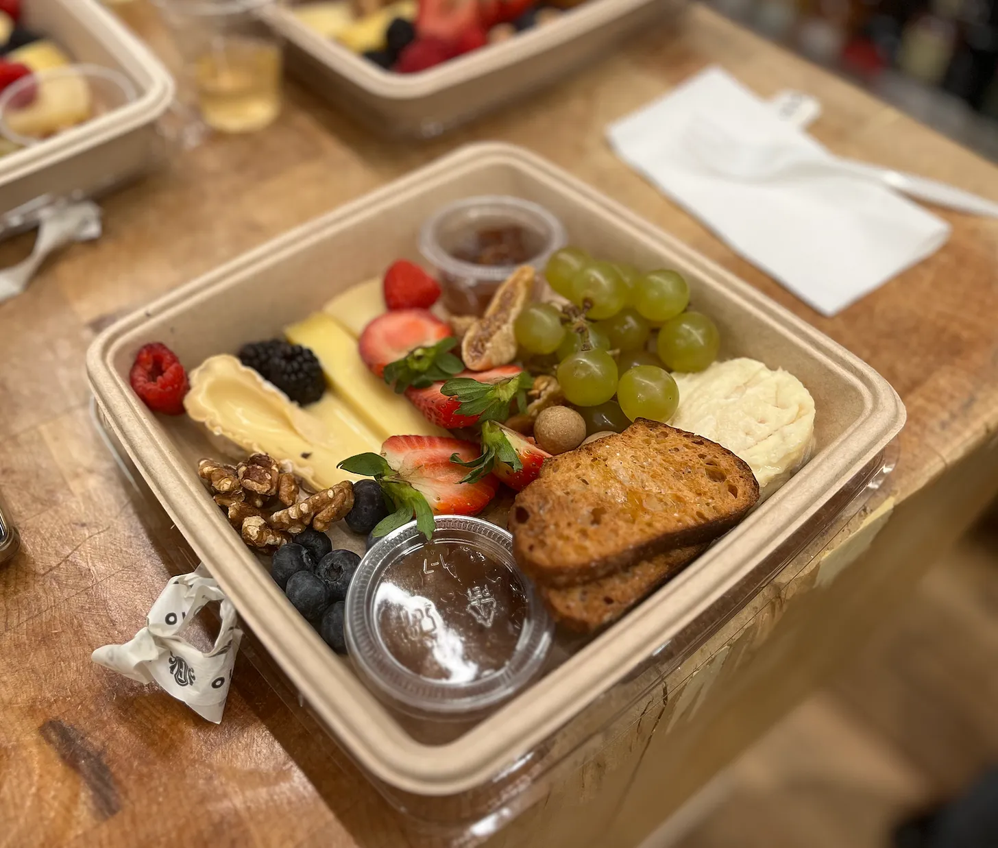 a picture of a plate filled with assorted cheese, berries, grapes, toast, jam, walnuts from Formaggio Kitchen on a butcher block