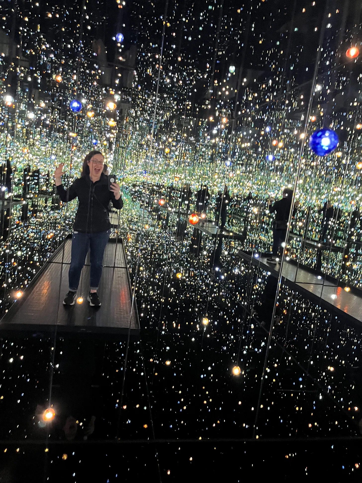 Sam tackeff standing in a darkened room filled with thousands of pinpoints of light and mirrored walls by the artist yayoi kusama