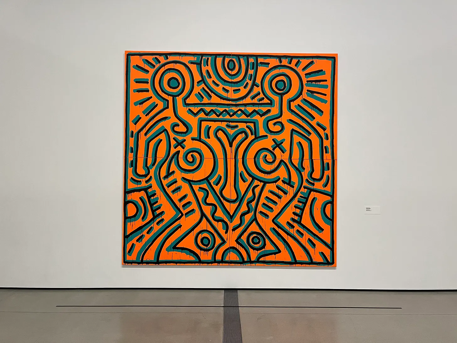 a large square orange canvas of art with stylized lines drawn by the artist Keith Haring