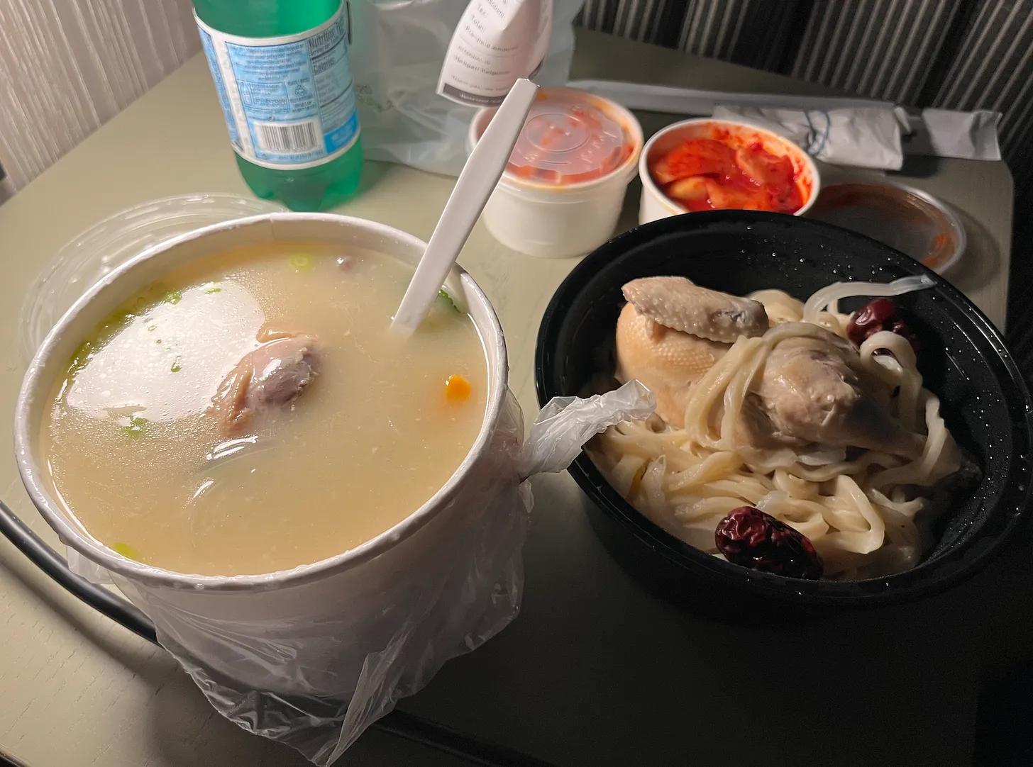 several bowls on a small table of food including soup, and chicken and noodles, kimchi, and a bottle of san pellegrino 